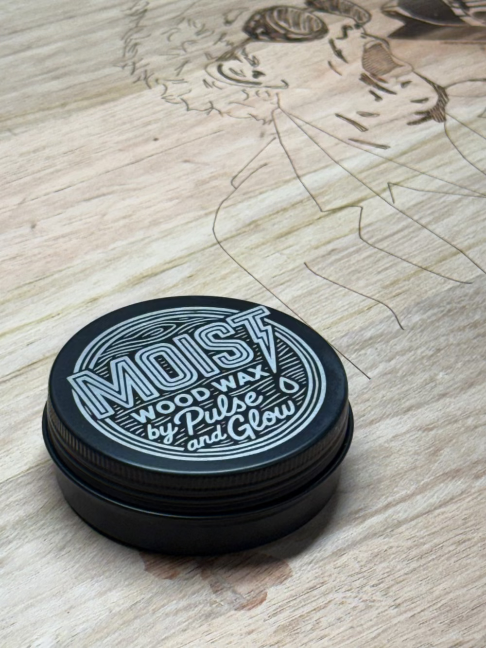 Black container lid with 'MOIST Wood Wax' text on a wooden surface with a drawing.